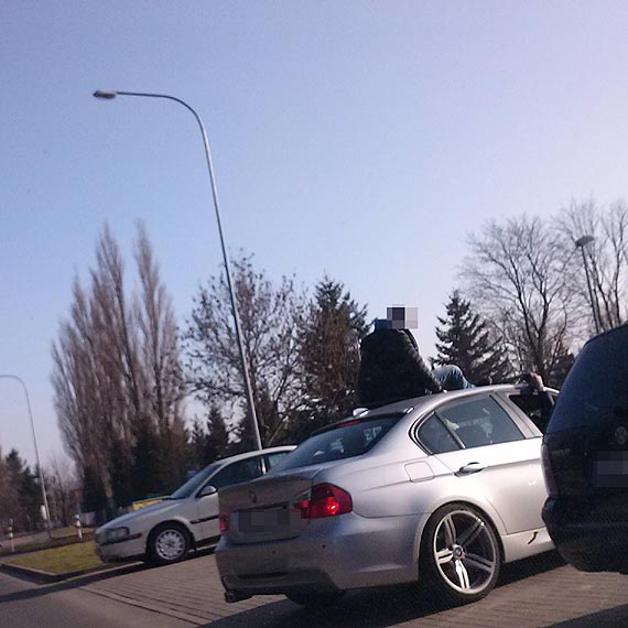 Idiota jedzi na dachu BMW i macha do ludzi